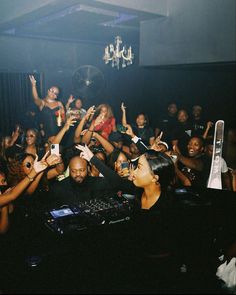 a group of people at a party with dj's in the background holding up their hands