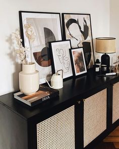 a black and white sideboard with pictures on it, vases and lamp in the corner