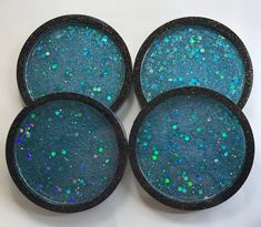 four blue glitter coasters sitting on top of a white tablecloth covered table with green and blue speckles