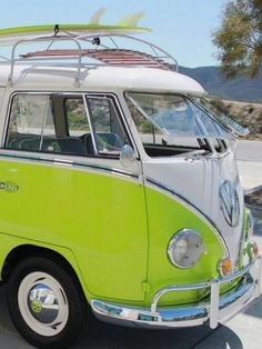 a green and white vw bus parked in a parking lot with a surfboard on top