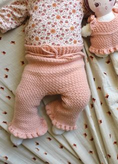 a baby doll laying on top of a bed next to a stuffed animal toy in pink pants