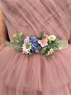 a woman wearing a pink tulle dress with flowers and greenery on the waist