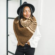 a woman wearing a knitted scarf and hat standing in front of a ladder with her hands on her hips