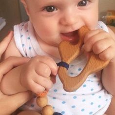 a baby is holding a wooden toy in its mouth and chewing on it's teeth