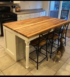 a kitchen island with stools and a wooden table top in front of an oven