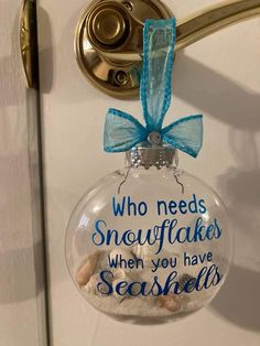 a glass ornament hanging on a door with a blue ribbon and saying who needs snowflakes when you have seashells