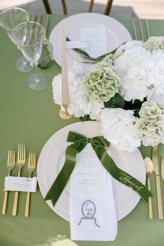 the table is set with white flowers and green napkins, gold cutlery, and silverware