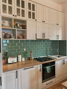 a kitchen with white cabinets and green subway tile backsplash, wood counter tops