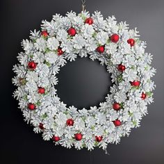 a christmas wreath with white flowers and red berries hanging on a wall in front of a black background