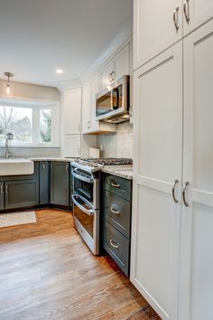 Kitchen remodel with white upper cabinets, a grey backsplash, light granite countertops, new vinyl plank flooring, and farm sink under the bay window White Upper Cabinets Light Grey Lower, White Top Cabinets Grey Lower, Grey Plank Flooring, Gray Farmhouse Sink With White Cabinets, Apron Front Kitchen Sink Stainless Steel, Stainless Still Apron Sink Woth Blue Cabinets