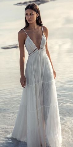 a woman standing in the water wearing a white dress with spaghetti straps and open back