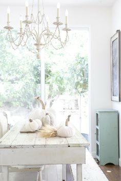 a dining room table with white pumpkins on it and candles hanging from the chandelier