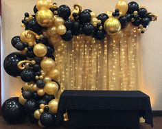 black and gold balloons are on display in front of a curtain with lights behind it