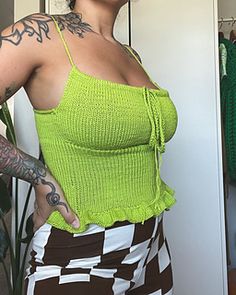 a woman with tattoos standing in front of a mirror wearing a green top and checkered skirt