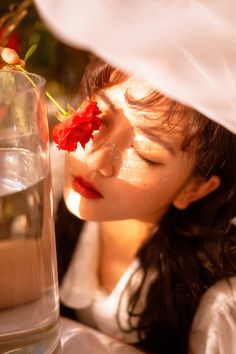 a woman holding a flower in her hand next to a vase filled with water and sand