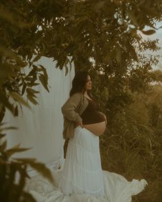 a pregnant woman in a white dress standing under a tree