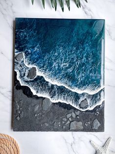 an aerial view of the ocean with rocks and plants next to it on a marble surface