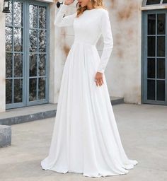 a woman wearing a white wedding dress standing in front of a building with large windows