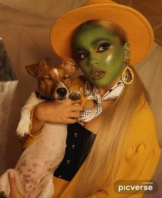 a woman with green makeup holding a dog