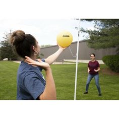 two women playing frisbee on the grass in front of a building and one is holding a yellow ball