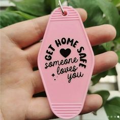 a hand holding a pink keychain that says, get home safe someone loves you