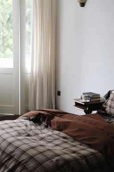 a bed sitting in front of a window next to a wooden table with books on it