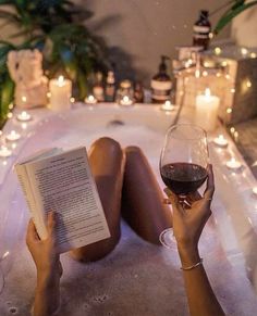 a woman laying in a bathtub reading a book and holding a glass of wine