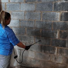 a woman is painting a brick wall with black paint on the walls and holding a sprayer