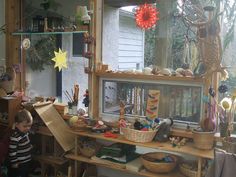 a young boy standing in front of a wooden shelf filled with lots of toys and knick knacks