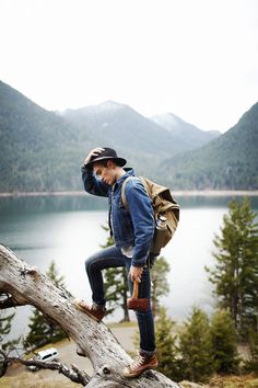 a man standing on top of a tree branch next to a lake with mountains in the background