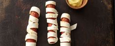 three hot dogs wrapped in strips of paper next to a bowl of mayonnaise