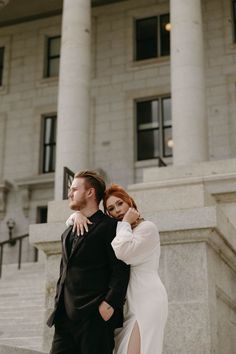 a man and woman standing next to each other in front of a building with columns