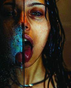 a woman sticking her tongue out behind a glass door with water on it's face