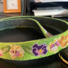 a close up of a cell phone on a table with a flowered belt around it