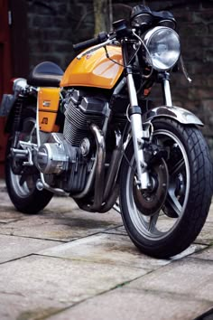 a yellow motorcycle parked on top of a stone floor next to a brick wall and door