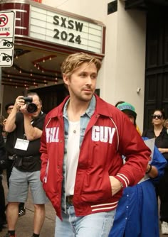 a man is walking down the street in front of a movie theater and taking pictures