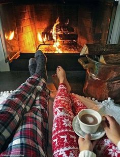 two people sitting in front of a fireplace with their feet up on the coffee cup