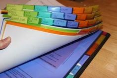 a person holding a stack of folders on top of a tabletop with sticky notes attached to it