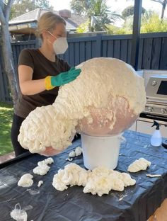 a woman wearing a face mask and gloves is making a sculpture out of dough on a table