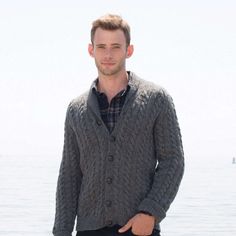 a man standing in front of the ocean wearing a gray cardigan