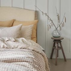 a bed with plaid sheets and pillows on top of it next to a small table