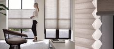 a woman standing next to a window with shades on it