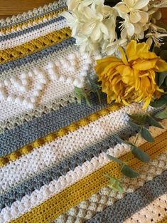 a crocheted blanket with yellow flowers on the floor next to it and a bouquet of flowers