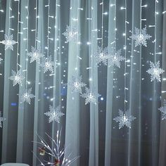 snowflakes are hanging from the curtain in front of a christmas tree with lights