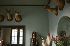 a woman standing in front of a wall with deer heads on the wall and flowers