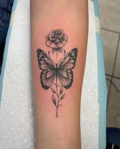 a black and white tattoo with a rose on the left side of the arm that has a butterfly in it