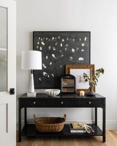 a black table topped with a basket next to a lamp and framed art on the wall