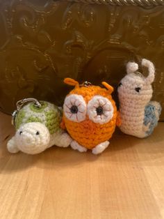 three small crocheted animals sitting next to each other on a wooden table with a metal object in the background