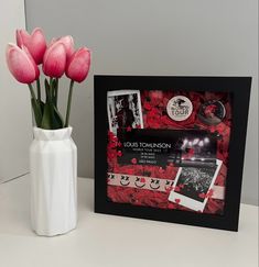 there is a vase with pink flowers in it next to a card and photo frame