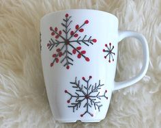 a white coffee cup with red and black snowflakes on it sitting on a fluffy surface